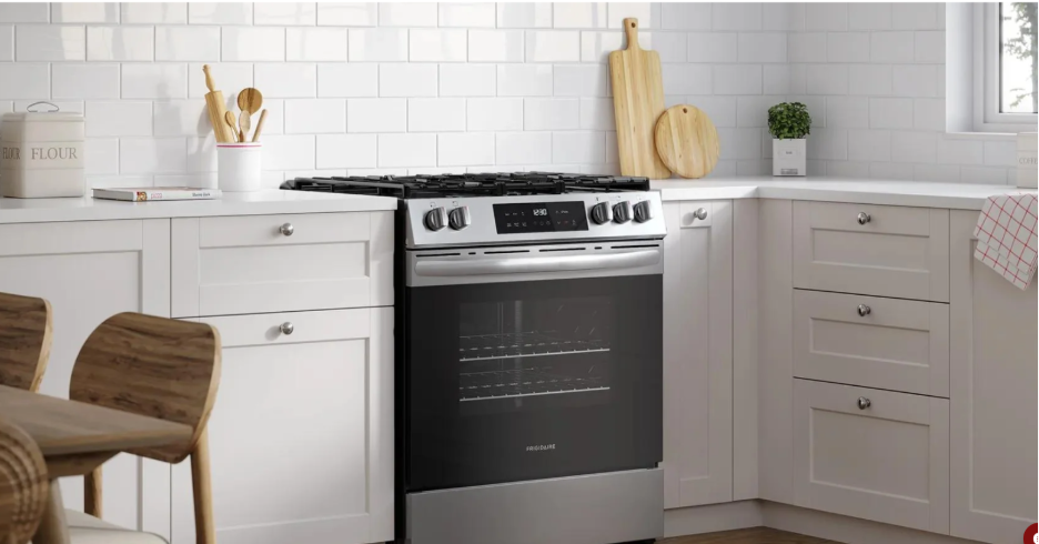 Gas stove with a stainless steel finish and black oven in a modern white kitchen with subway tile backsplash and wooden utensils.